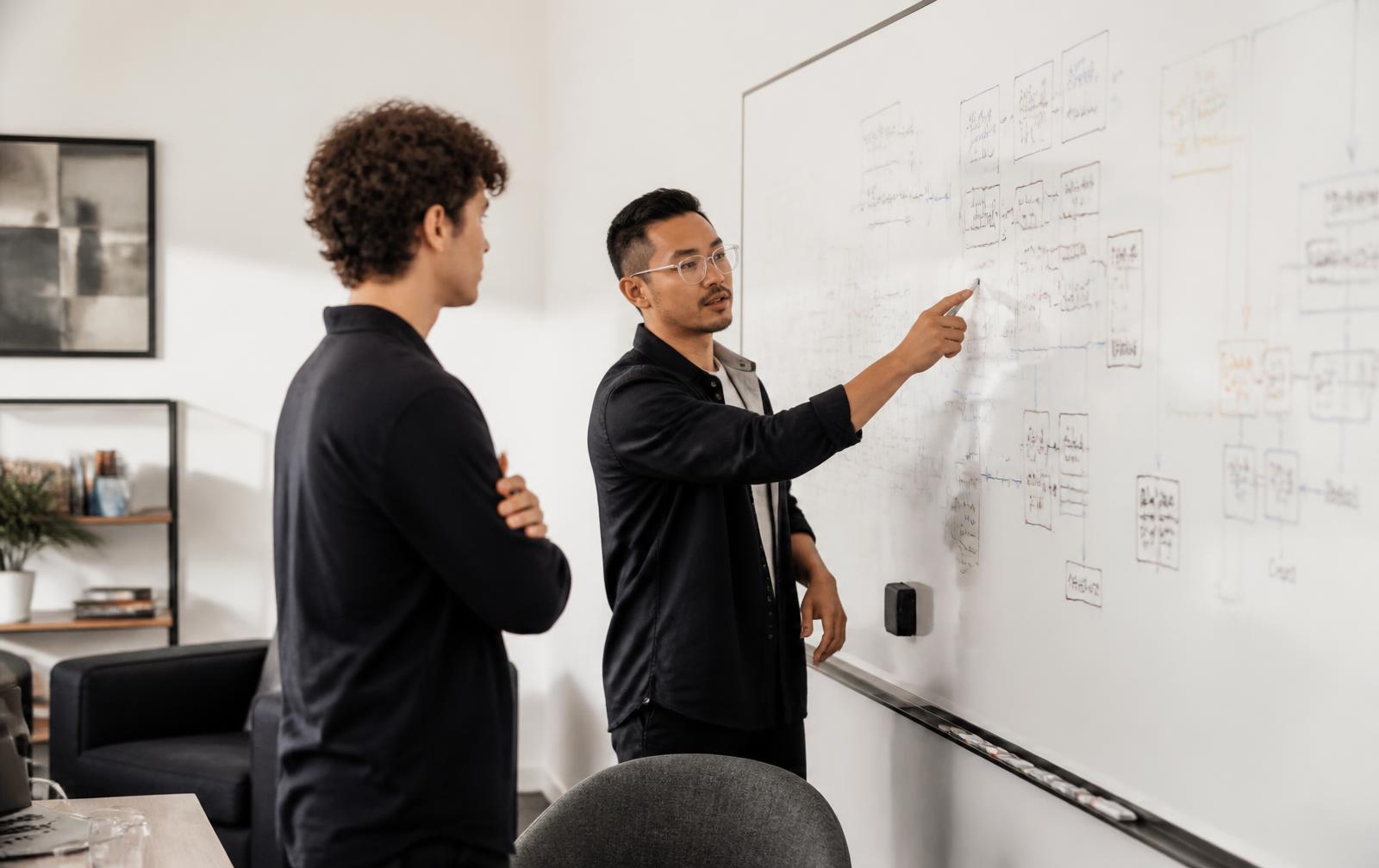 Two engineers discussing a system architecture diagram drawn on a large whiteboard